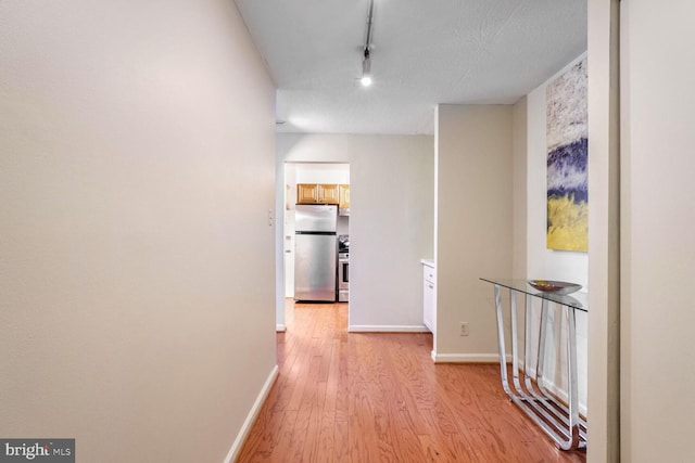 hall featuring light wood-type flooring, track lighting, and a textured ceiling