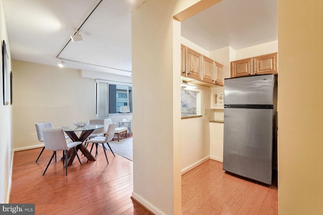 kitchen with light brown cabinets, stainless steel fridge, track lighting, and light wood-type flooring