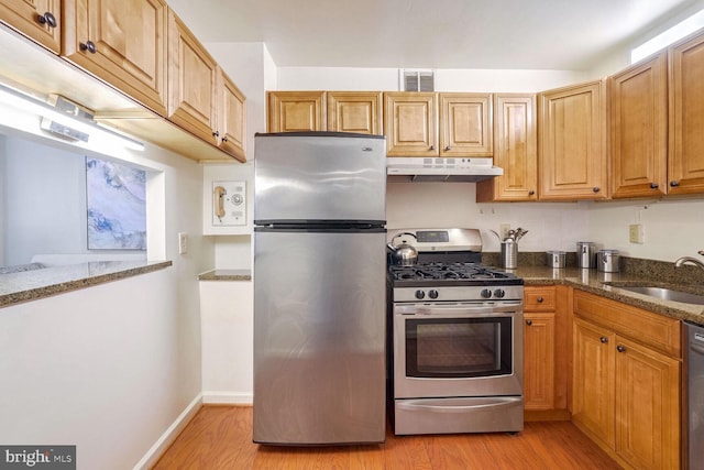 kitchen featuring appliances with stainless steel finishes, light hardwood / wood-style flooring, dark stone counters, and sink