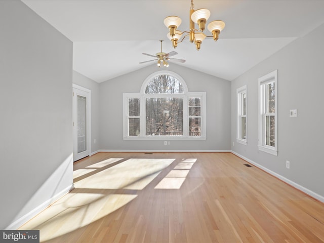 unfurnished dining area with lofted ceiling, a wealth of natural light, ceiling fan with notable chandelier, and light wood-type flooring