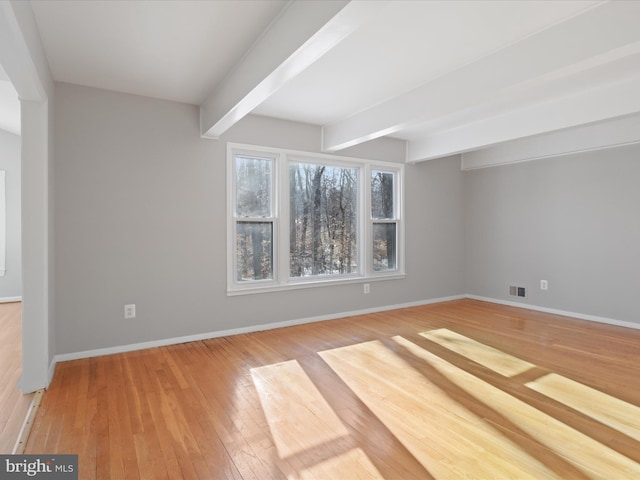 empty room featuring light hardwood / wood-style floors and beamed ceiling