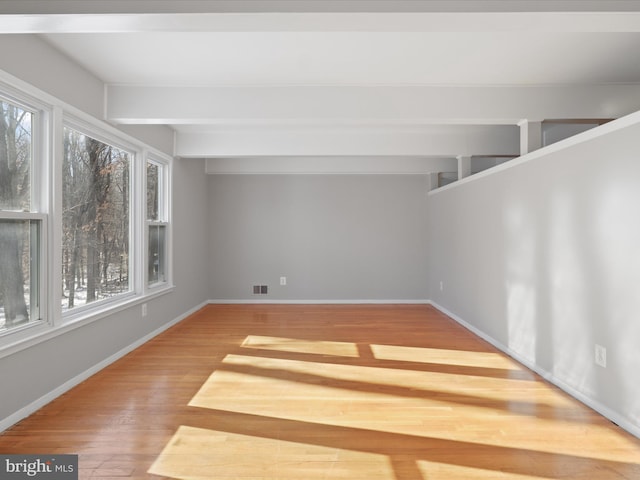 empty room featuring beamed ceiling, plenty of natural light, and hardwood / wood-style floors