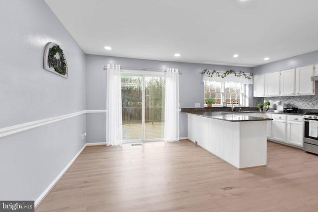 kitchen with stainless steel stove, tasteful backsplash, white cabinetry, kitchen peninsula, and light wood-type flooring