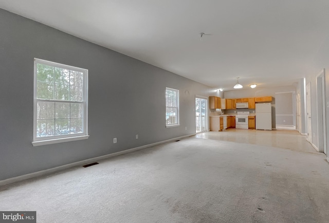 unfurnished living room featuring light carpet and a wealth of natural light