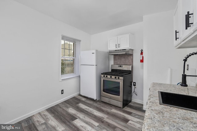 kitchen with hardwood / wood-style floors, white refrigerator, light stone countertops, white cabinetry, and stainless steel range with gas stovetop