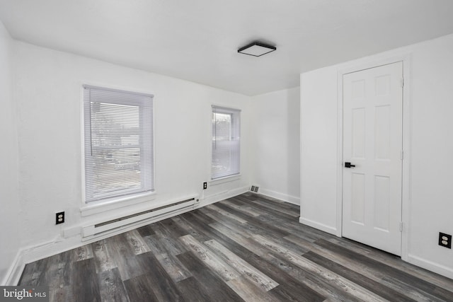 spare room featuring baseboard heating and dark hardwood / wood-style floors