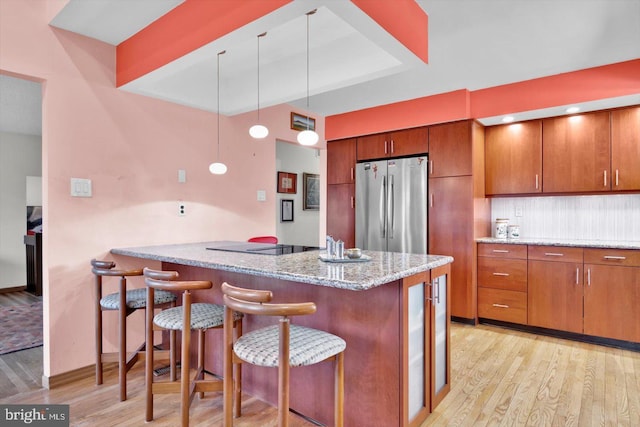 kitchen with light hardwood / wood-style flooring, kitchen peninsula, decorative backsplash, hanging light fixtures, and stainless steel fridge