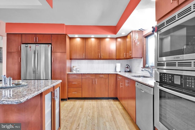 kitchen featuring sink, light wood-type flooring, decorative backsplash, light stone countertops, and appliances with stainless steel finishes