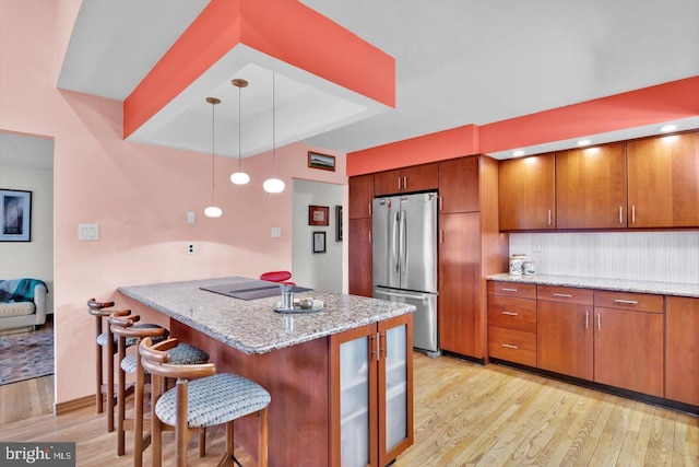 kitchen with hanging light fixtures, light wood-type flooring, kitchen peninsula, a breakfast bar, and stainless steel fridge