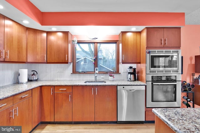 kitchen with stainless steel appliances, sink, light hardwood / wood-style flooring, decorative backsplash, and light stone countertops