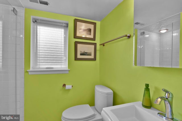 bathroom with sink, tiled shower, a wealth of natural light, and toilet