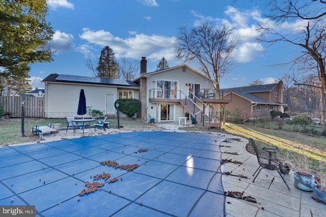 rear view of house featuring a balcony, a covered pool, a patio area, and solar panels