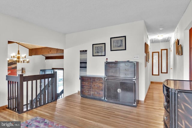 interior space with a textured ceiling, beamed ceiling, light hardwood / wood-style flooring, and a chandelier