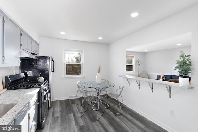 kitchen featuring stainless steel gas stove, gray cabinetry, dark hardwood / wood-style flooring, light stone counters, and backsplash