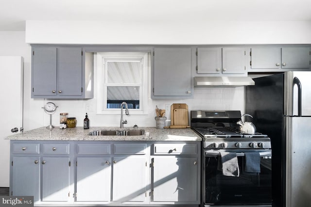 kitchen featuring stainless steel fridge, gray cabinets, backsplash, range with gas stovetop, and sink