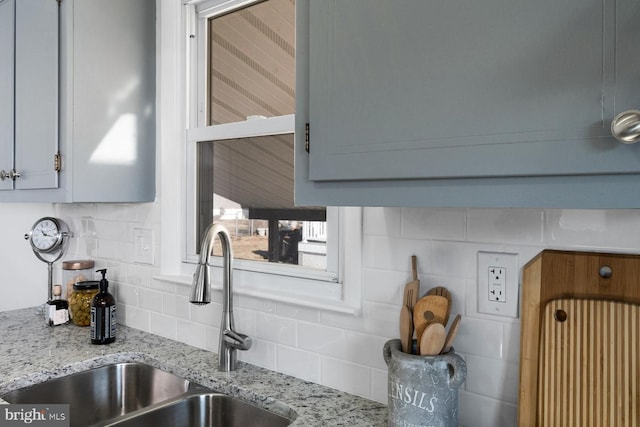 room details featuring sink, light stone counters, backsplash, and gray cabinets