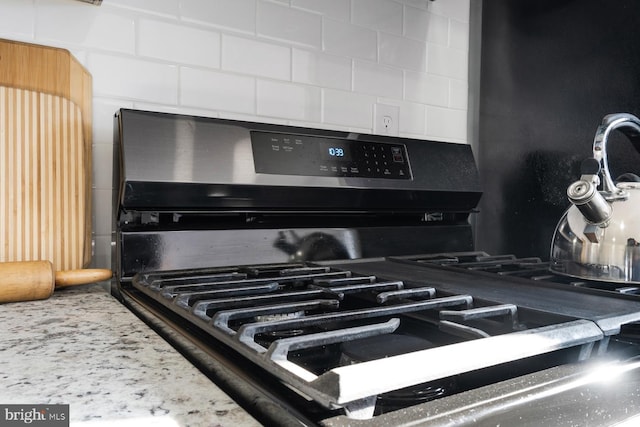 details with light stone counters, gas range, and decorative backsplash