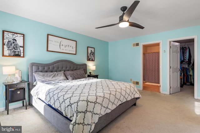 bedroom with ceiling fan, light colored carpet, a walk in closet, and ensuite bath