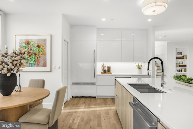 kitchen with dishwashing machine, paneled refrigerator, white cabinets, sink, and light hardwood / wood-style flooring