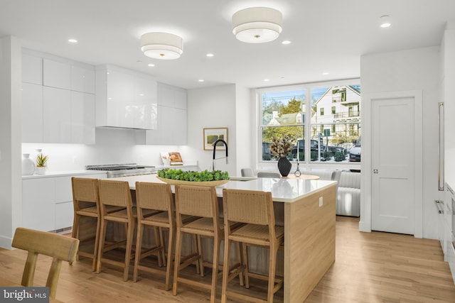 kitchen with a breakfast bar, white cabinets, light hardwood / wood-style flooring, and an island with sink