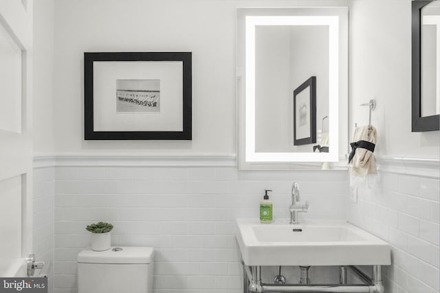 bathroom featuring toilet, tile walls, and sink