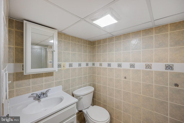 bathroom featuring vanity, toilet, tile walls, and a drop ceiling