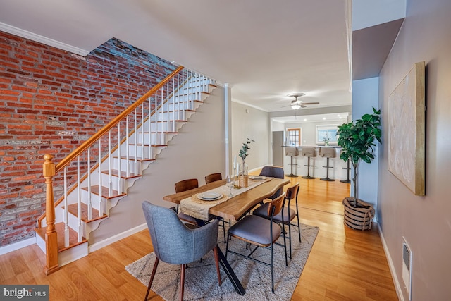 dining space with crown molding, brick wall, ceiling fan, and light hardwood / wood-style floors