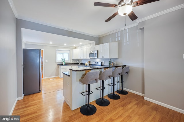 kitchen featuring a breakfast bar area, appliances with stainless steel finishes, kitchen peninsula, light hardwood / wood-style floors, and white cabinets