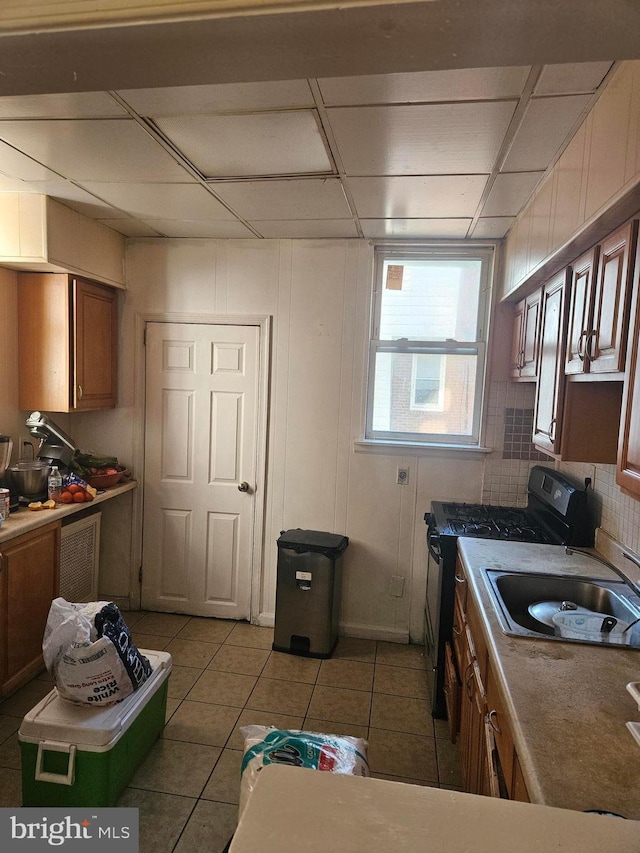 kitchen featuring a paneled ceiling, light tile patterned flooring, black gas stove, and sink