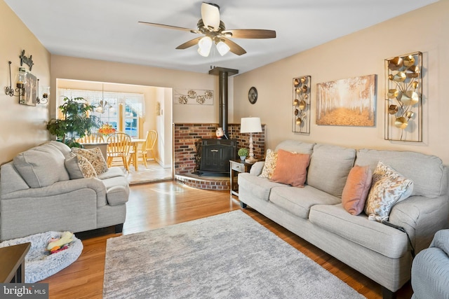 living room with ceiling fan, a wood stove, and hardwood / wood-style floors