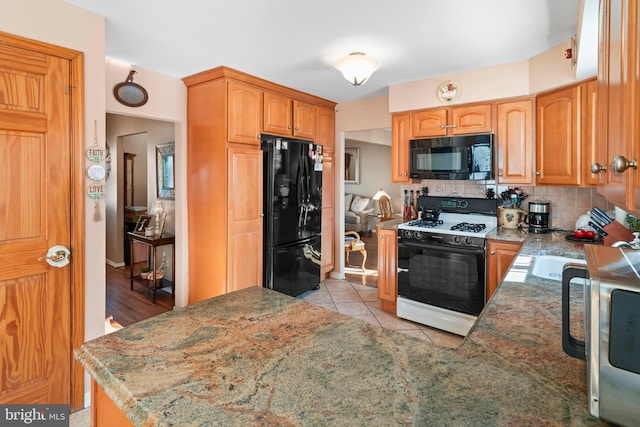 kitchen featuring kitchen peninsula, backsplash, light tile patterned floors, light stone countertops, and black appliances