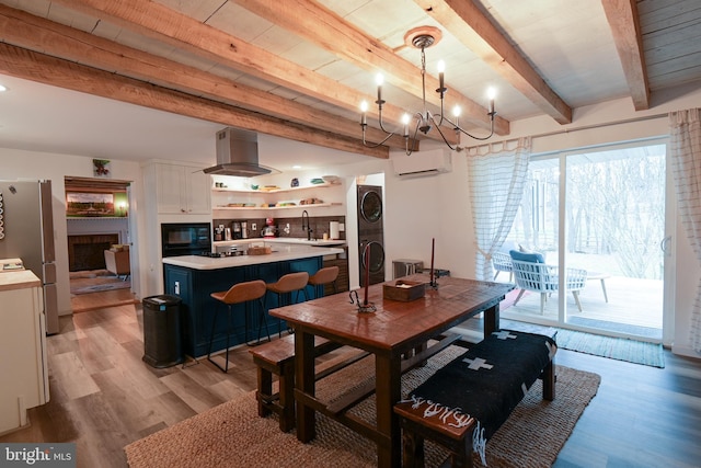 dining space featuring stacked washer and dryer, light wood finished floors, a wall unit AC, beamed ceiling, and a chandelier