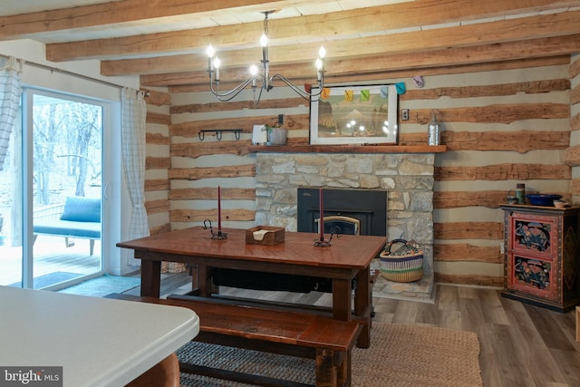 dining area featuring a stone fireplace, wood finished floors, beam ceiling, and a notable chandelier