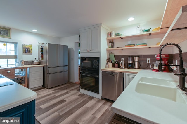 kitchen with black appliances, light wood-style flooring, light countertops, and a sink