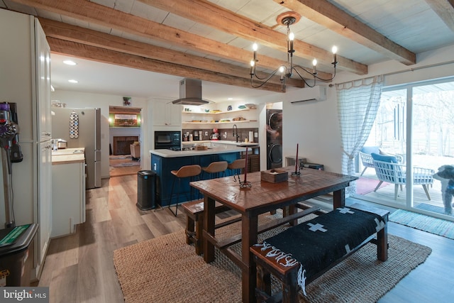 dining room featuring light wood-type flooring, an AC wall unit, beamed ceiling, and an inviting chandelier