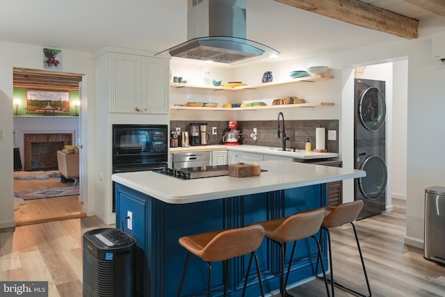 kitchen featuring tasteful backsplash, extractor fan, light countertops, stacked washing maching and dryer, and black microwave