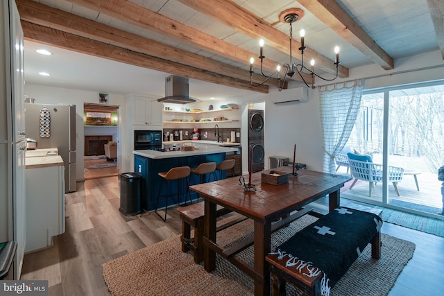 dining room featuring beam ceiling, a fireplace, light wood finished floors, stacked washer and dryer, and a wall mounted AC