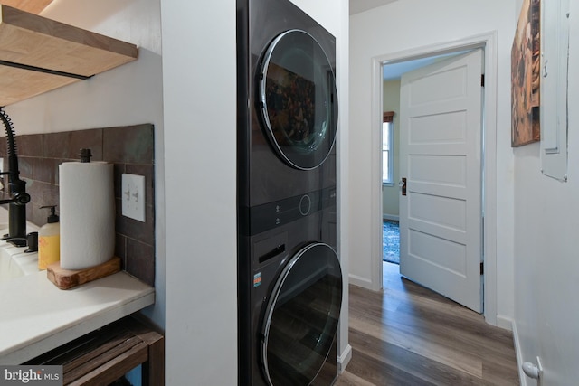 laundry room featuring stacked washer and dryer, wood finished floors, laundry area, and baseboards