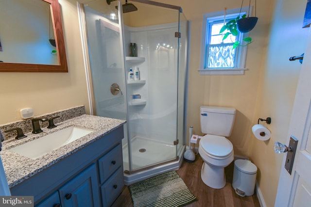 bathroom featuring baseboards, toilet, wood finished floors, vanity, and a shower stall