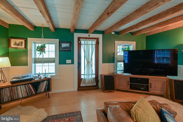 living area with beam ceiling, a wainscoted wall, and wood finished floors