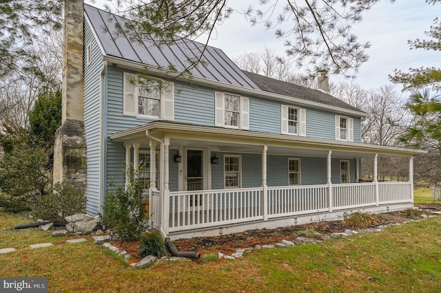 country-style home featuring covered porch, metal roof, a chimney, and a standing seam roof