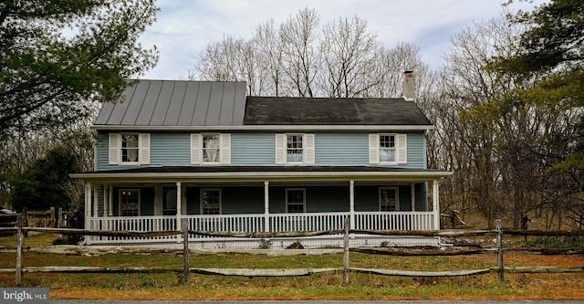 view of front of property with a chimney, metal roof, a standing seam roof, fence, and a porch