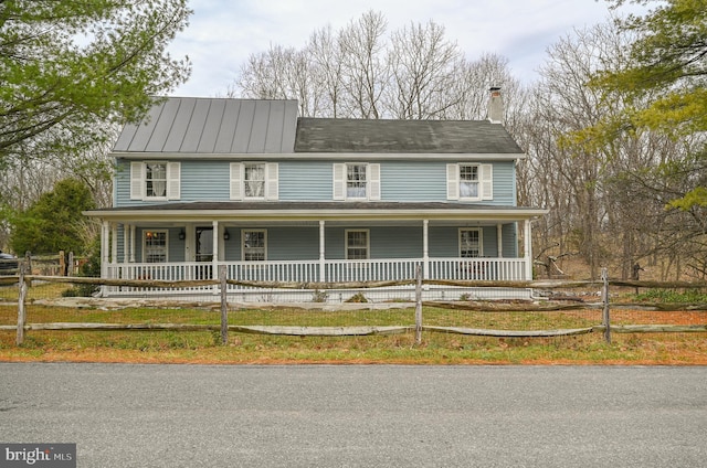 farmhouse-style home featuring a porch, a fenced front yard, and a chimney