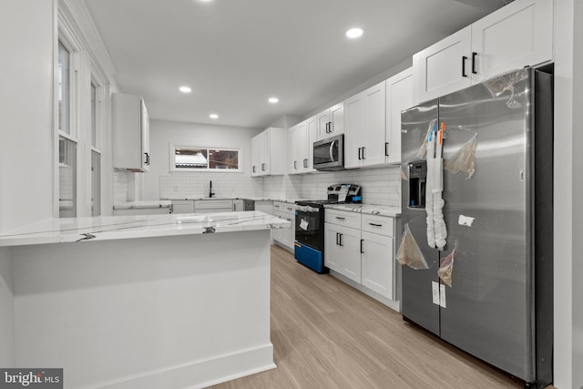 kitchen featuring light stone counters, kitchen peninsula, light hardwood / wood-style floors, white cabinets, and appliances with stainless steel finishes