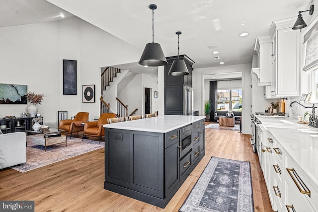 kitchen with light wood-type flooring, vaulted ceiling, pendant lighting, white cabinets, and a center island