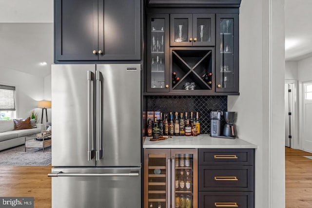 bar with tasteful backsplash, stainless steel refrigerator, beverage cooler, and light hardwood / wood-style flooring