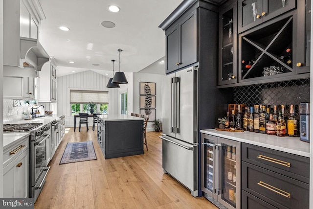 kitchen with premium appliances, wine cooler, pendant lighting, lofted ceiling, and light wood-type flooring