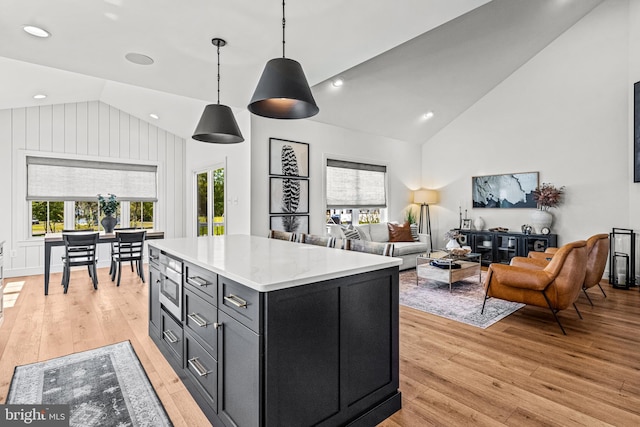 kitchen with built in microwave, hanging light fixtures, high vaulted ceiling, light hardwood / wood-style floors, and a kitchen island