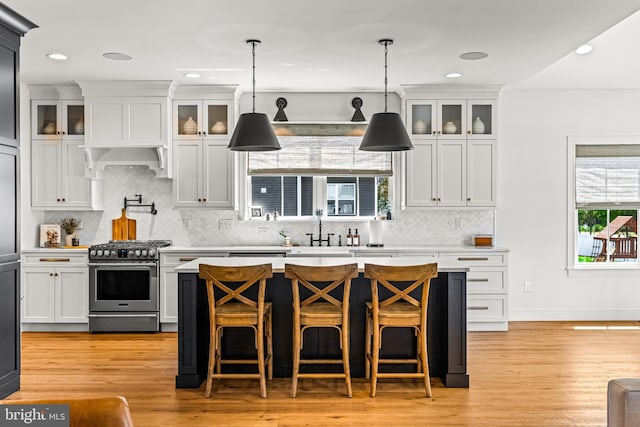 kitchen with sink, range hood, decorative light fixtures, white cabinetry, and stainless steel range with gas stovetop