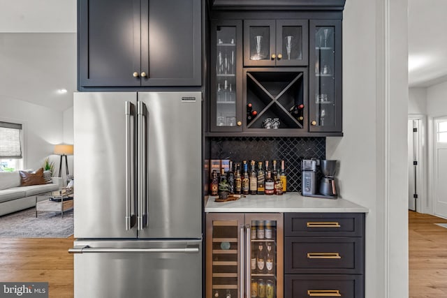 bar featuring backsplash, stainless steel fridge, light hardwood / wood-style flooring, and beverage cooler